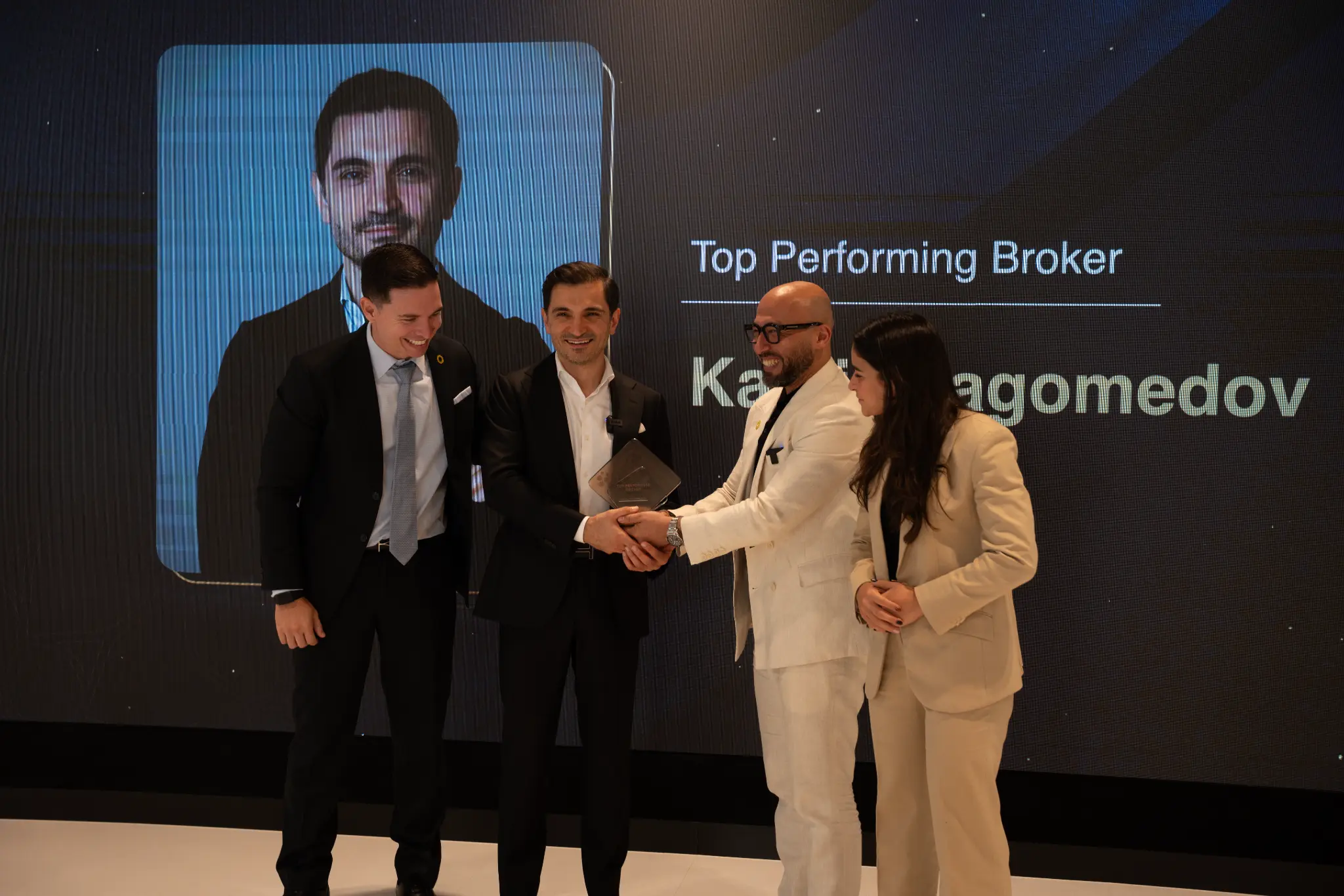 Kamil Magomedov on stage at the Expo City Dubai Top Performing Broker ceremony, holding the crystal award trophy with the Expo City team