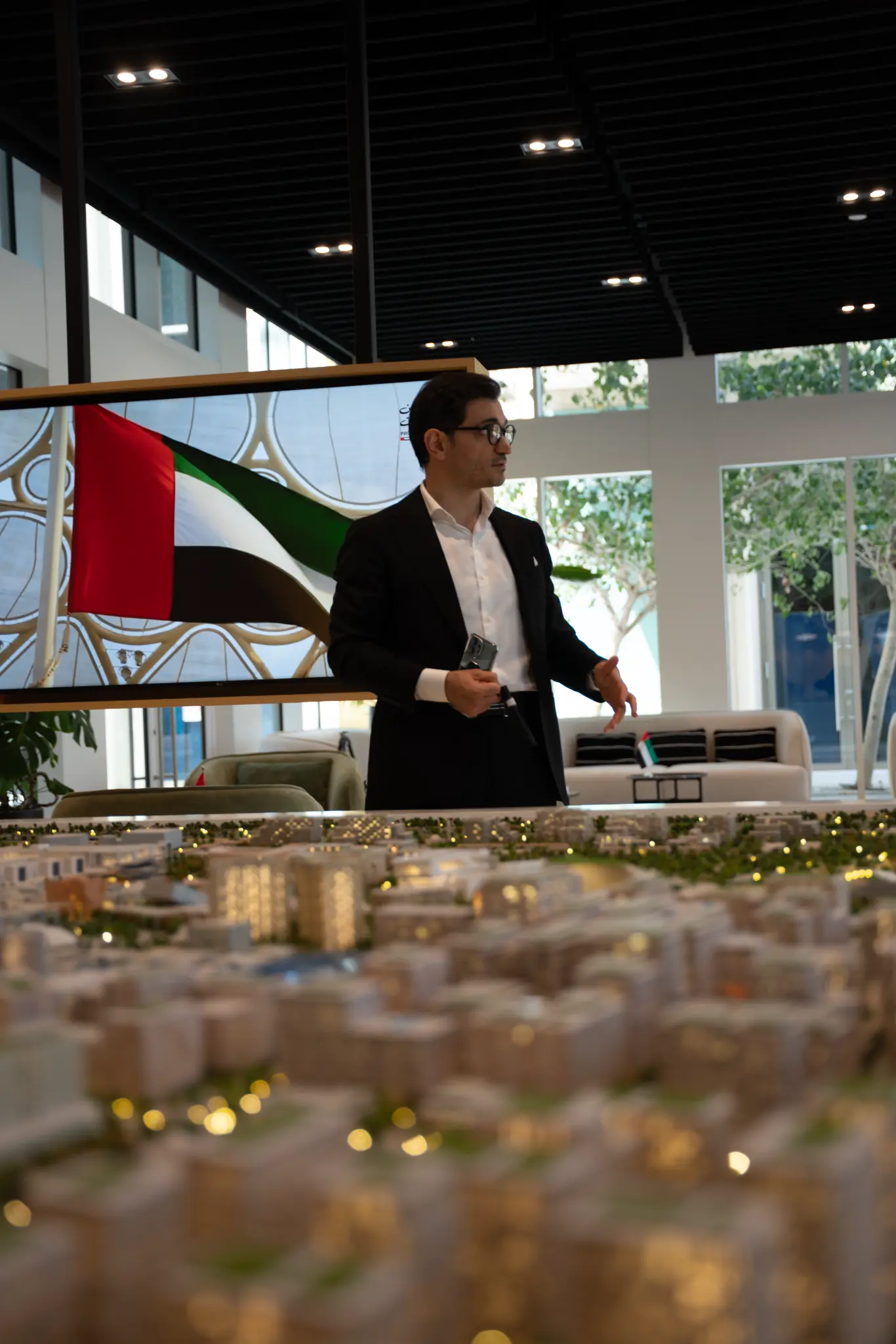 Kamil Magomedov standing at the Expo City Dubai sales centre with the UAE flag and architectural model in the foreground