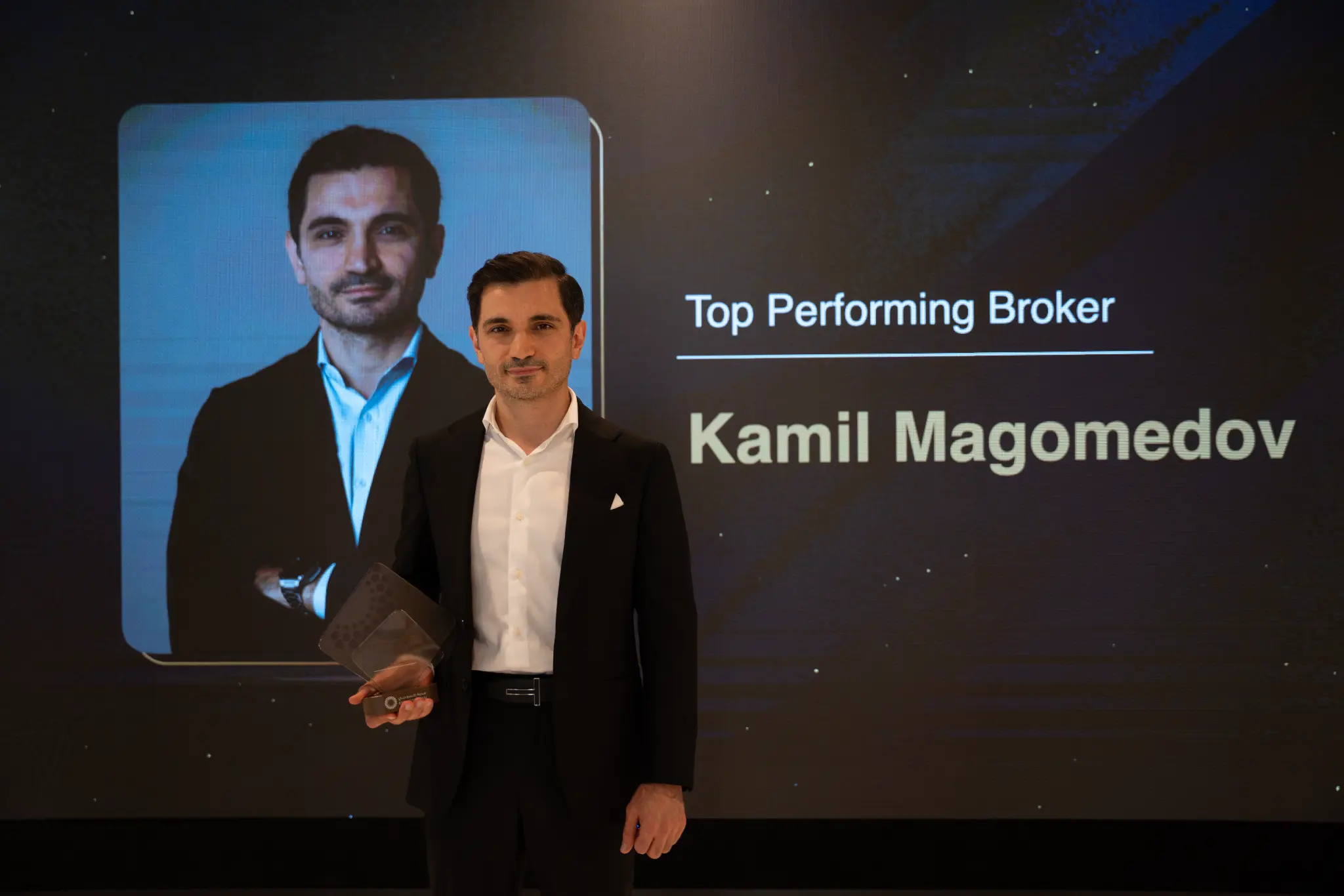 Kamil Magomedov receiving the Top Performing Broker award from Expo City Dubai on stage, with 'Top Performing Broker — Kamil Magomedov' displayed on the screen behind him